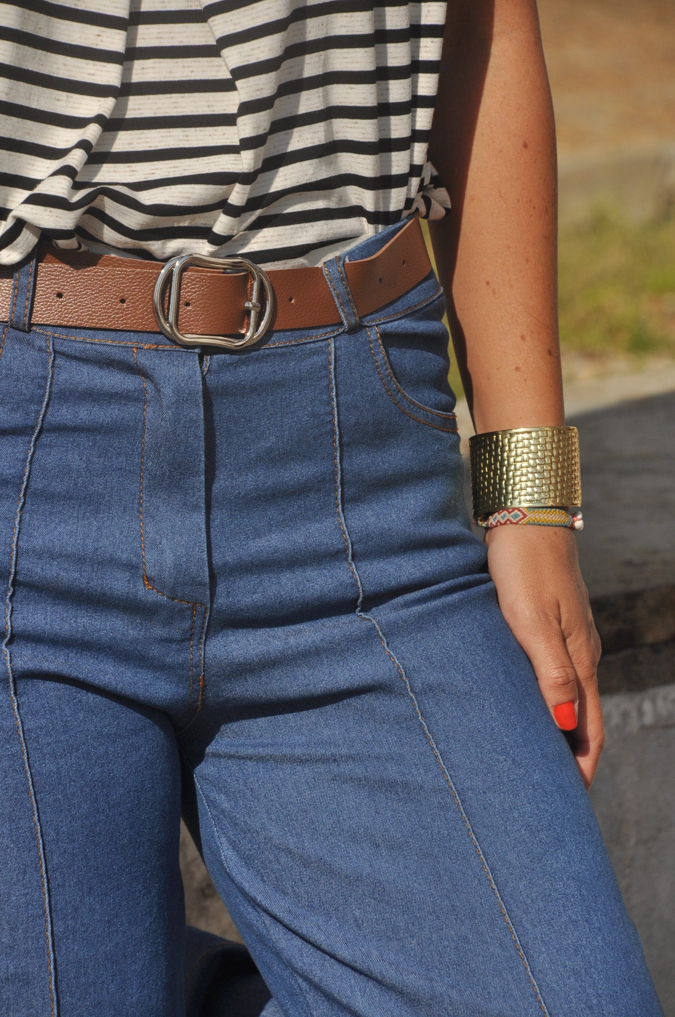 Gros plan sur la taille haute d'un pantalon jean large avec détails de surpiqûres verticales et ceinture marron.
