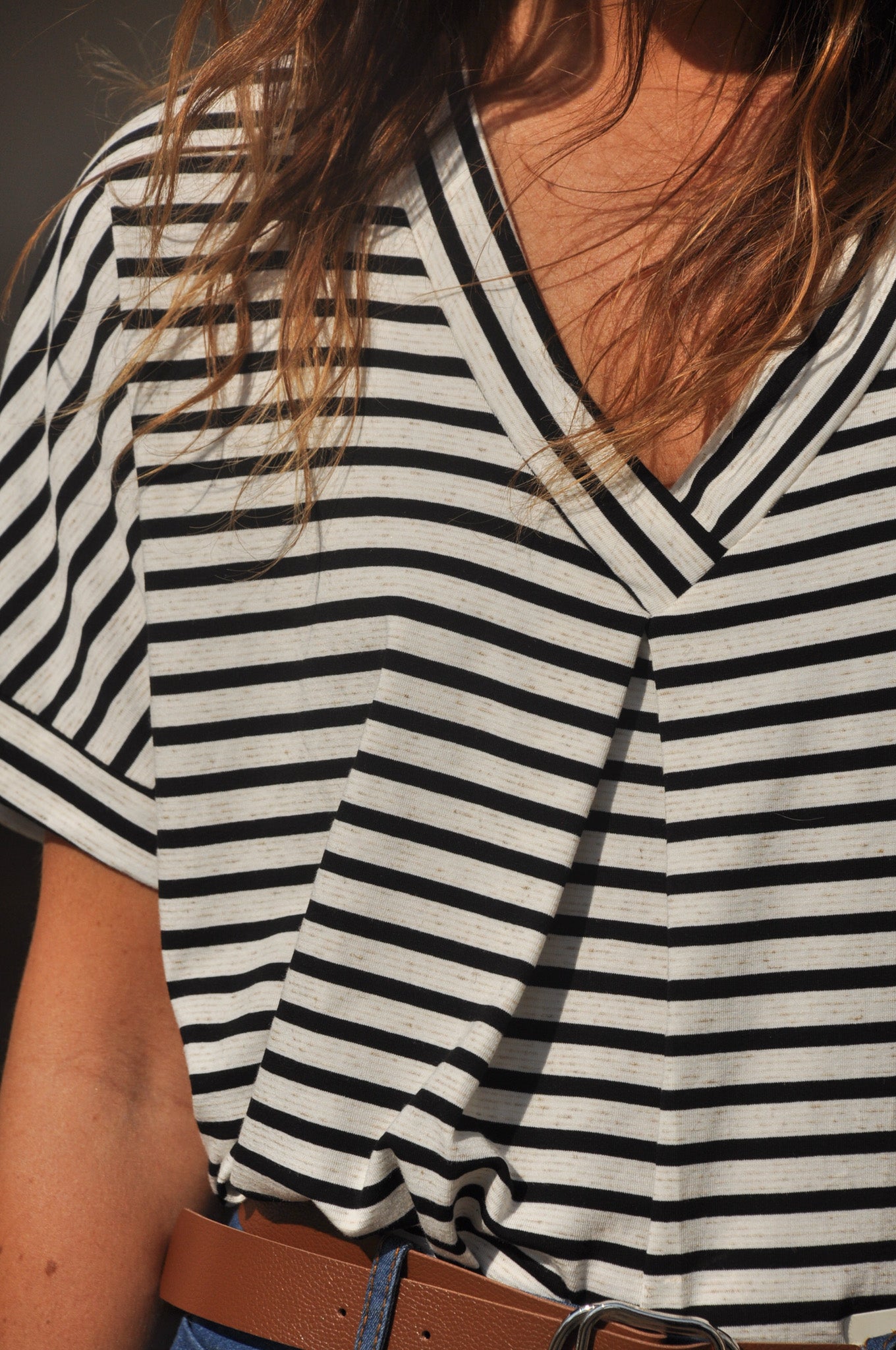 Femme portant un t-shirt marinière décontracté à rayures horizontales noires et blanches avec un jean et une ceinture marron.