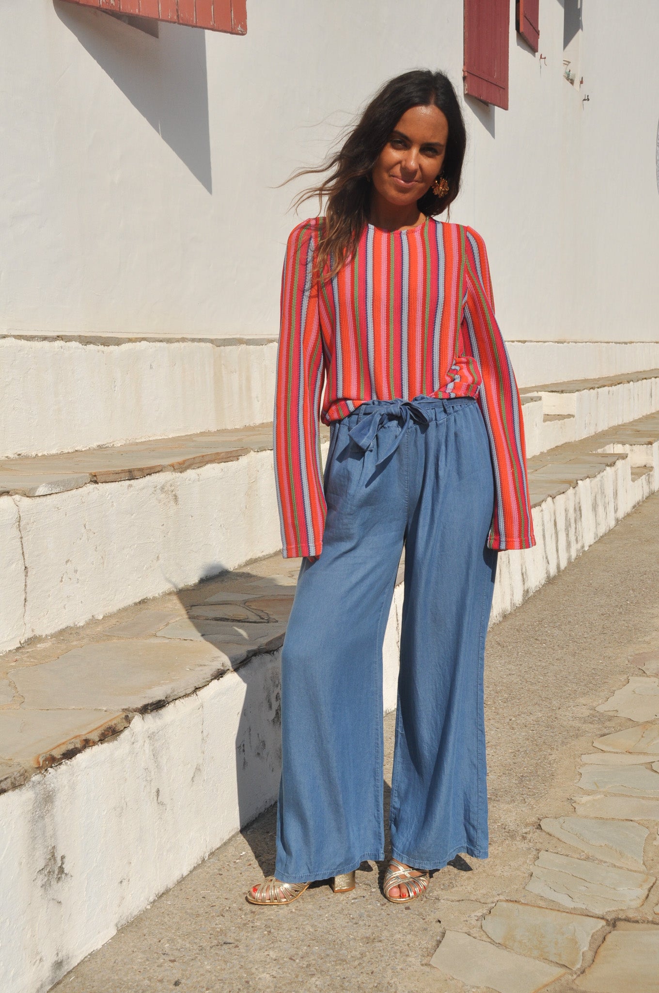 Femme souriante portant un pantalon large en jean fluide et un pull léger à rayures colorées