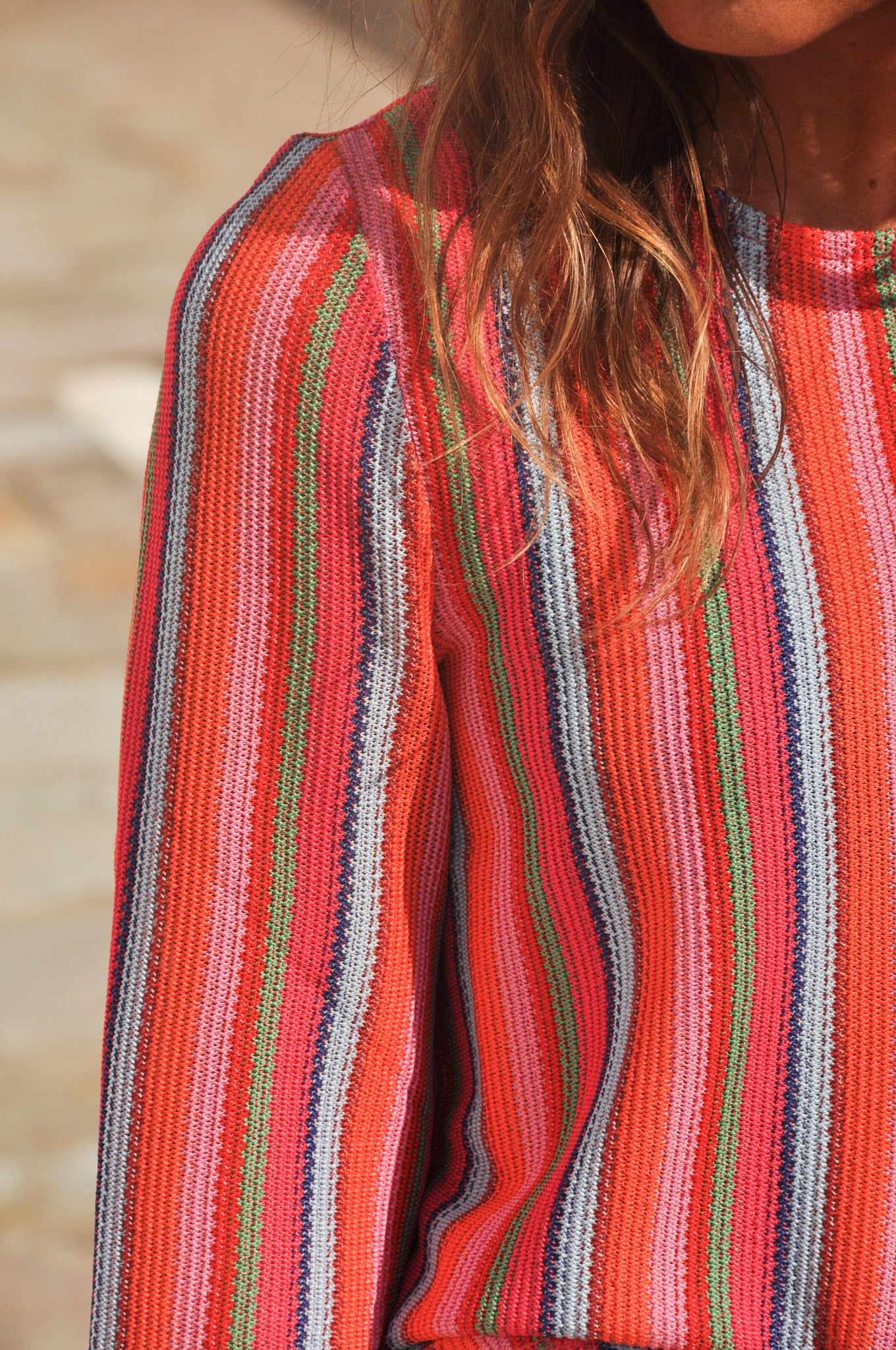 Gros plan sur la maille légère d'un pull à rayures verticales aux tons rouge, rose poudré, vert et gris