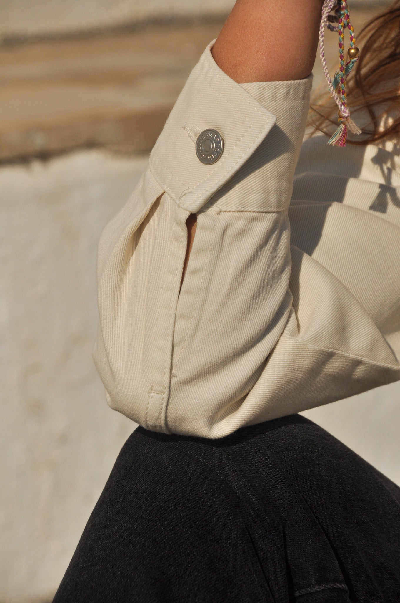 Détail de la manchette boutonnée de la veste denim écru à franges