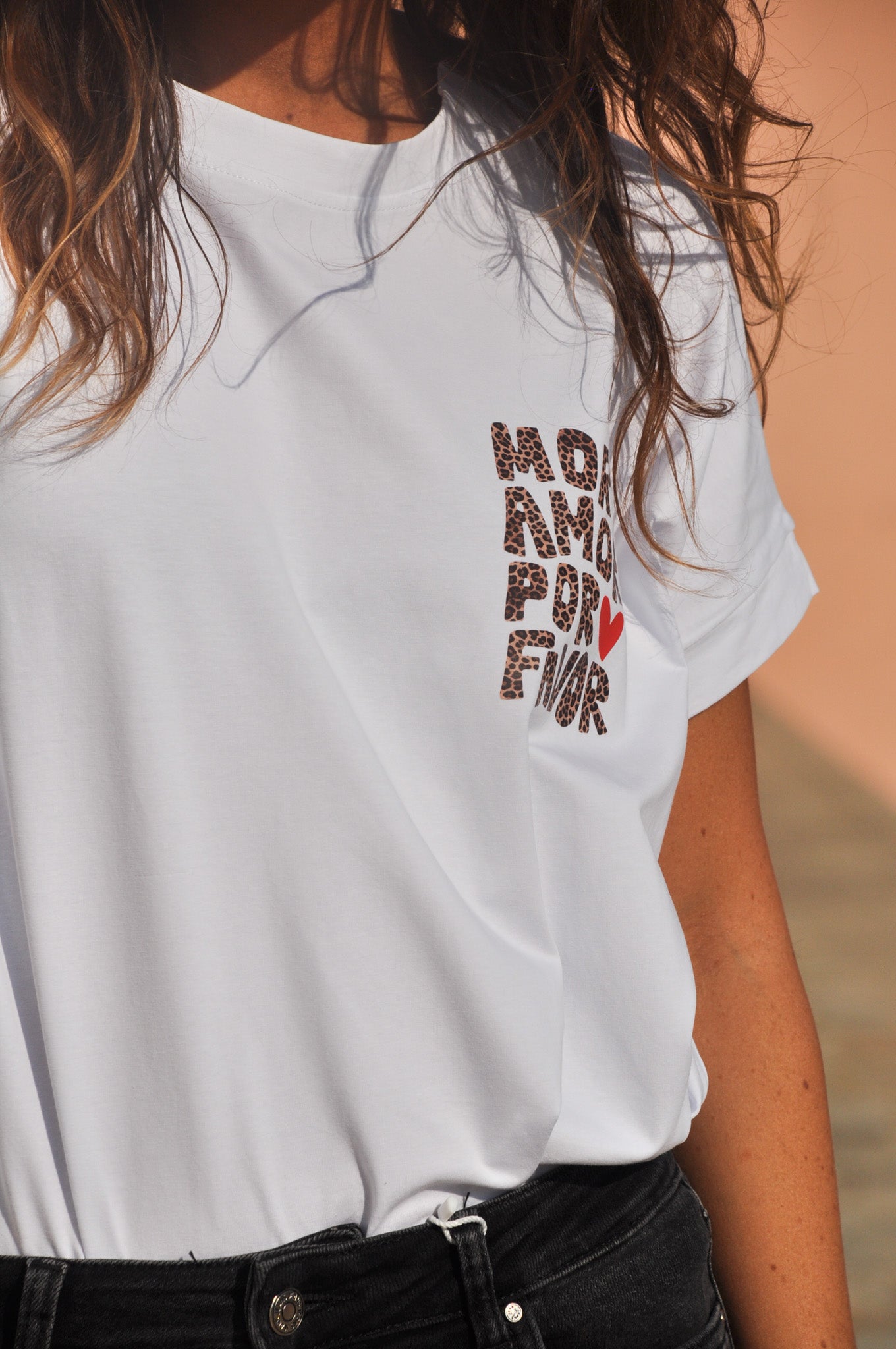 Gros plan sur l'avant d'un t-shirt blanc femme avec petit imprimé léopard 'More Amor Por Favor' et cœur rouge côté cœur.