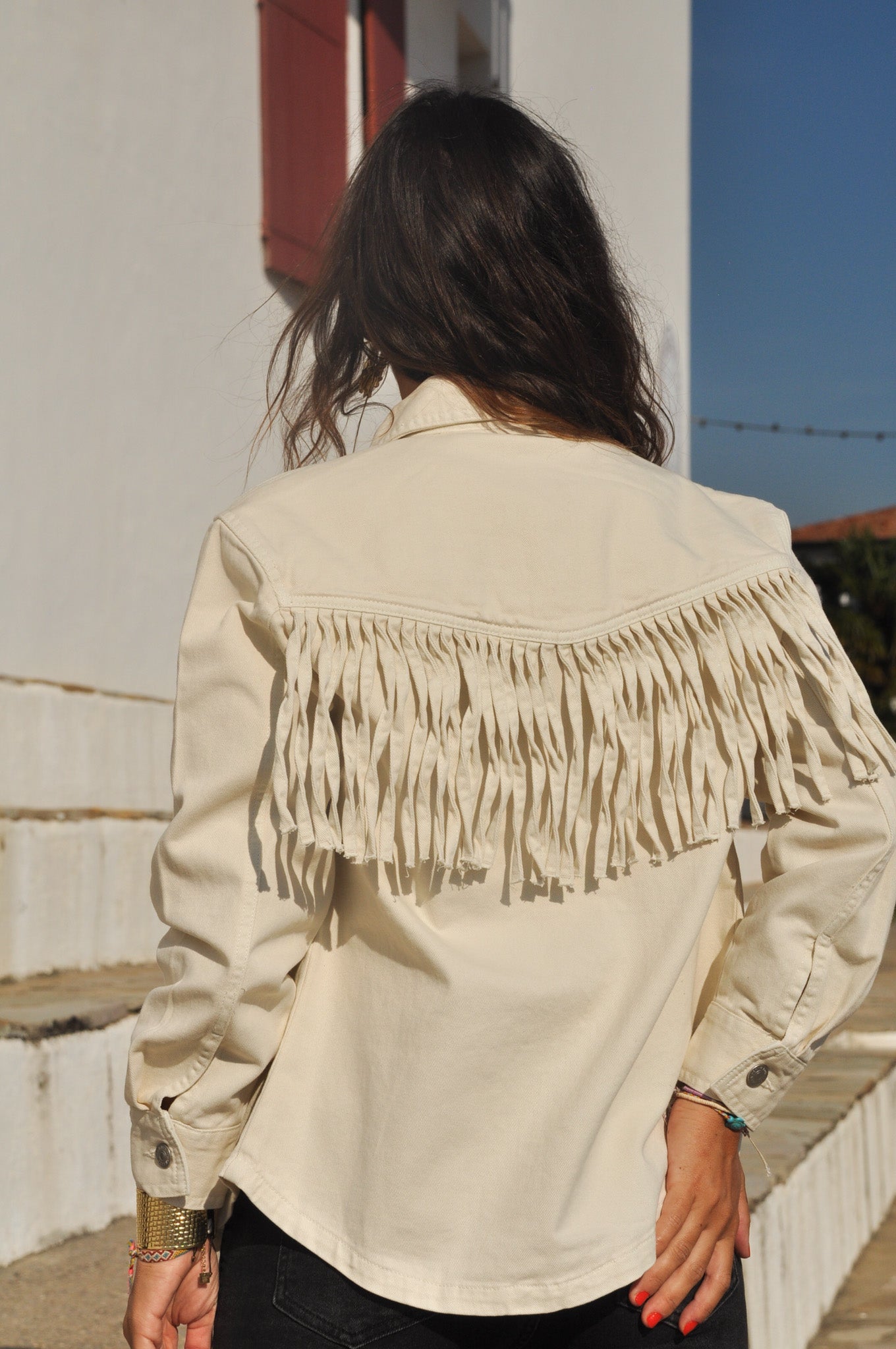 Femme vue de dos portant la veste denim écru avec ses franges dynamiques