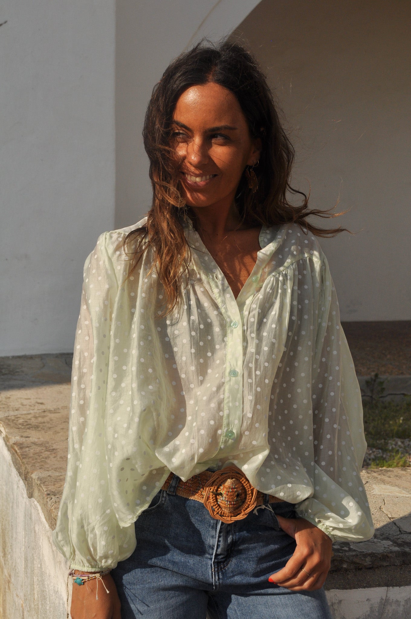 Femme souriante portant une blouse bohème fluide vert pastel à pois blancs et un jean